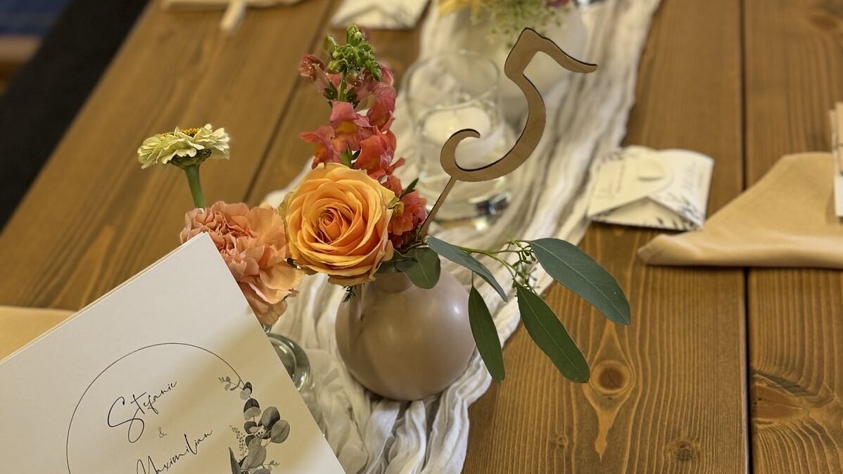 Festlich gedeckter Holztisch mit Blumen, Kerzen und Menükarte „Stefanie & Maximilian“ für eine Hochzeit.