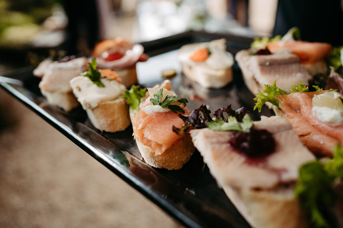 Elegante Auswahl an belegten Häppchen mit Lachs, Frischkäse und Kräutern auf Tablett angerichtet.