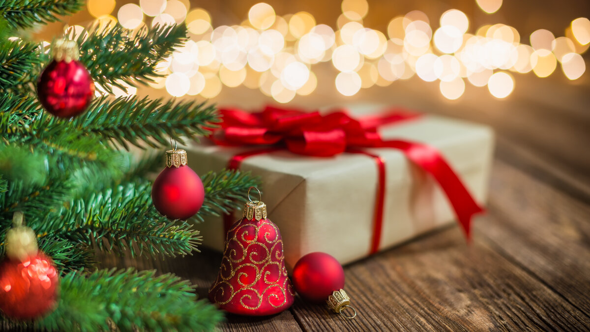 Weihnachtlich dekorierter Tannenbaum mit roten Kugeln und Geschenkbox vor warmem Lichterhintergrund.