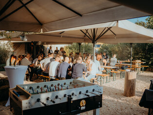 Blick in den Biergarten mit vielen Personen und im Vordergrund einem Tischkicker