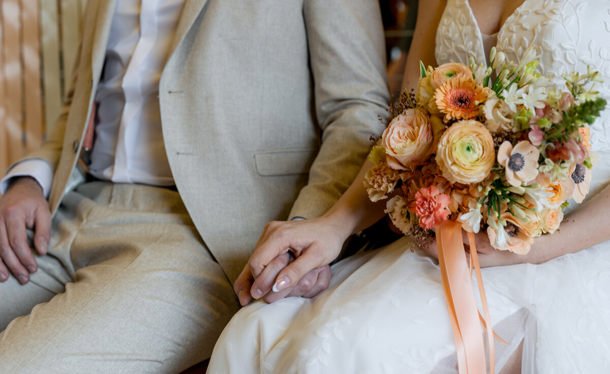 Nahaufnahme eines Paares in Hochzeitskleidung, das Händchen hält und einen Blumenstrauß zeigt.
