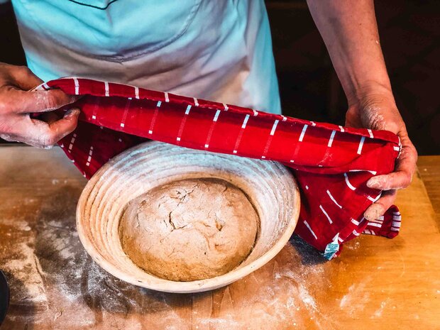 Teig in einem Brotkorb wird mit einem Tuch abgedeckt