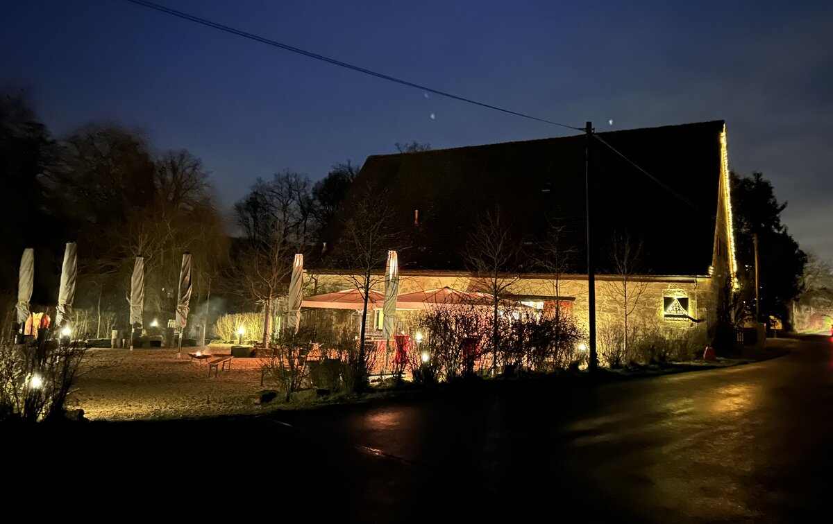 Außenansicht der festlich beleuchteten Kernmühle bei Nacht mit Terrasse, Heizstrahlern und Winterkulisse.