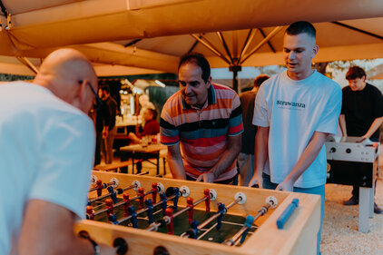 3 Männer spielen Tischkicker im Biergarten